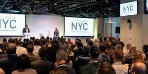a photo of two people standing on stage, infront of screens that read "BuildingEnergy NYC". There is a crowd infront of them, listening closely.